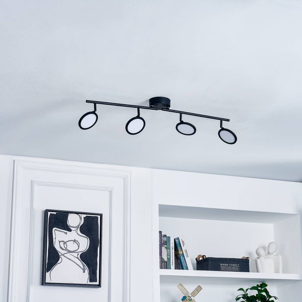 Moderne schwarze Deckenleuchte mit vier ringförmigen LED-Spots in einem hellen, minimalistisch eingerichteten Raum.