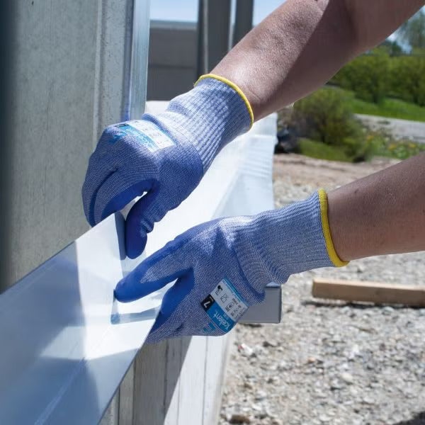 Eine Person trägt Arbeitshandschuhe bei der Handhabung eines Metallprofils im Außenbereich.