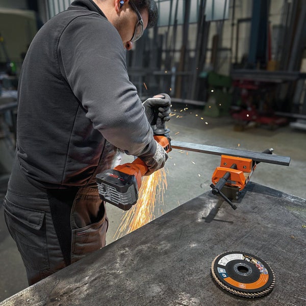 Handwerker bearbeitet Metall mit einem Akku-Winkelschleifer in einer Werkstatt, Funkenflug bei der Metallbearbeitung.