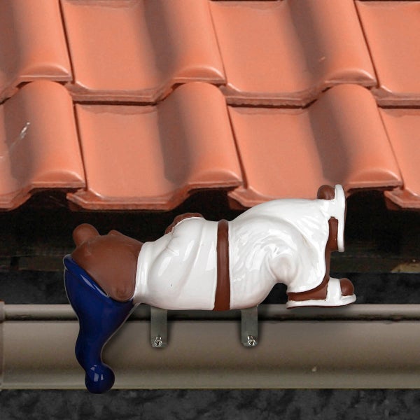 Dekorative Dachrinnenfigur eines liegenden Zwergs montiert an einer Regenrinne unter einem Ziegeldach.
