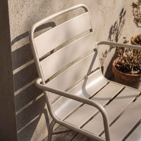 Moderner Gartenstuhl aus Metall mit Armlehnen und Latten-Design an einer Hauswand im Außenbereich.
