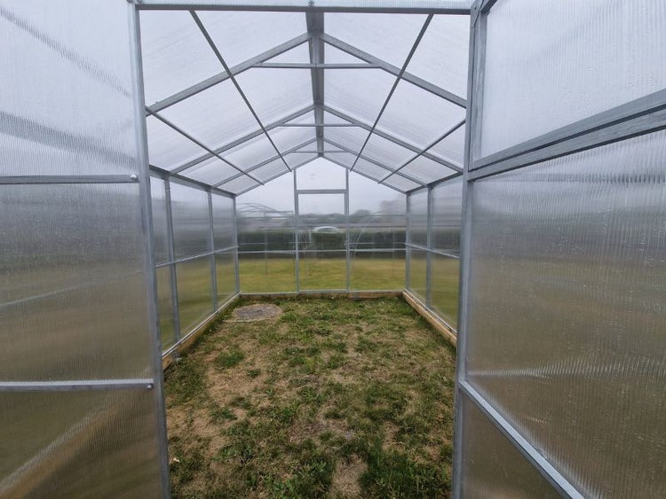 Innenansicht eines Gewächshauses mit Polycarbonatplatten und Metallrahmen.