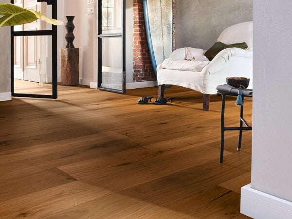 Wohnraum mit verlegtem Parkettboden in Holzoptik, kombiniert mit einem Sessel und rustikalem Wanddesign in einem hellen, modernen Interieur.