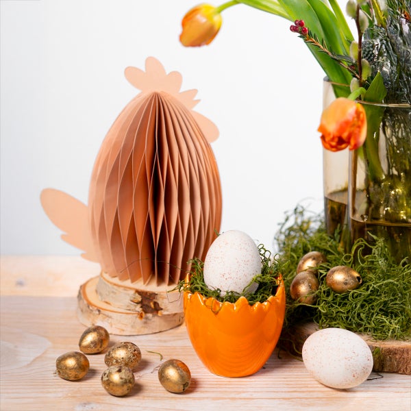 Dekorative Osterszene mit Papierhuhn, Blumenvase und Eiern auf einem Holztisch.