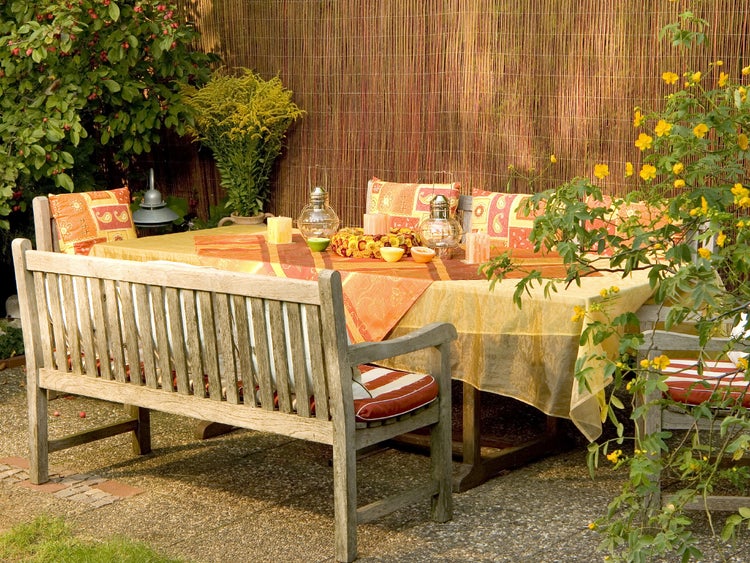 Gartenszene mit Esstisch, Bänken, Tischdecke und Dekoration für entspannte Stunden im Freien