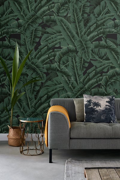 Dekoratives Wohnzimmer mit grüner Blättertapete, Sofa, Zierkissen, Beistelltisch und Zimmerpflanze.