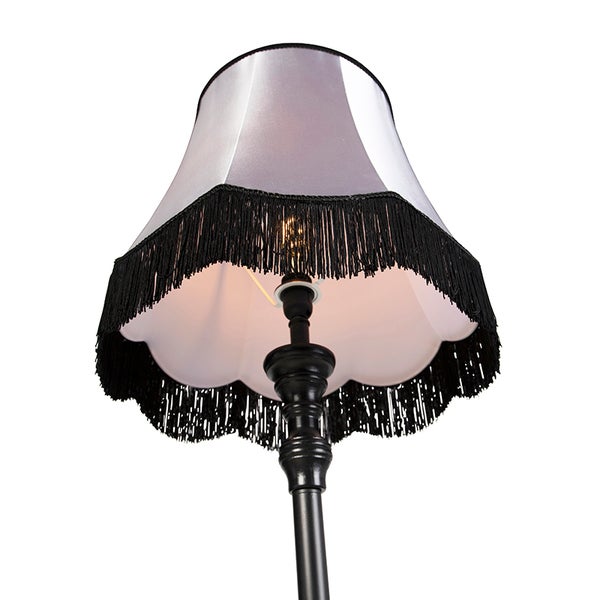 Stehleuchte im Vintage-Stil mit weißem Textilschirm, schwarzen Fransen und schwarzem Metallfuß.