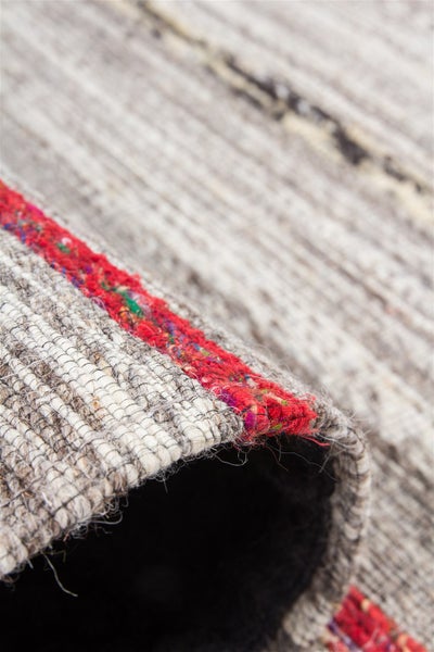 Detailansicht eines gewebten Teppichs mit grober Struktur und einem roten Randstreifen.
