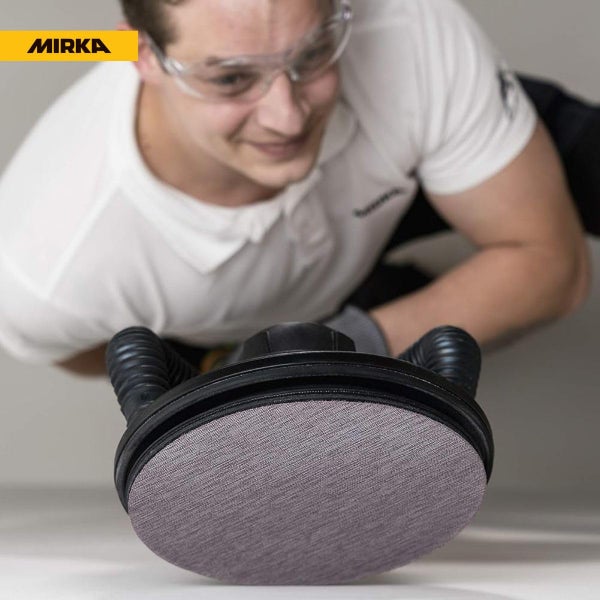 Ein Handwerker mit Schutzbrille bedient einen Mirka Exzenterschleifer mit Absaugvorrichtung für Schleifarbeiten.