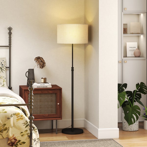 Moderne Stehleuchte mit zylindrischem Lampenschirm in einem gemütlich eingerichteten Schlafzimmer neben einem Nachttisch.