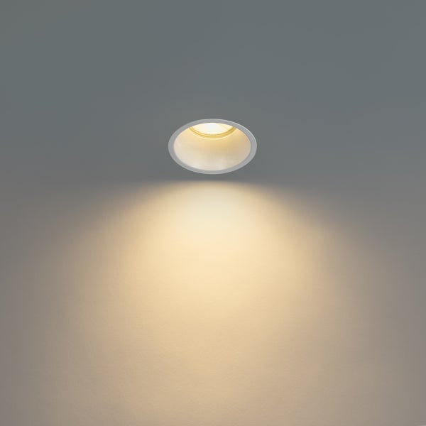 Runder LED Einbaustrahler mit warmweißem Lichtkegel an einer Wand.