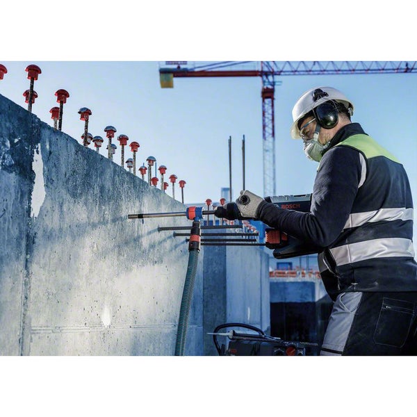 Ein Bauarbeiter bohrt mit einem Bohrhammer Löcher in eine Betonwand auf einer Baustelle.