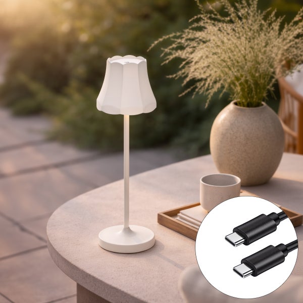 Weiße tragbare Tischleuchte mit wellenförmigem Schirm auf einem Gartentisch, inklusive USB C Ladekabel in der Detailansicht.