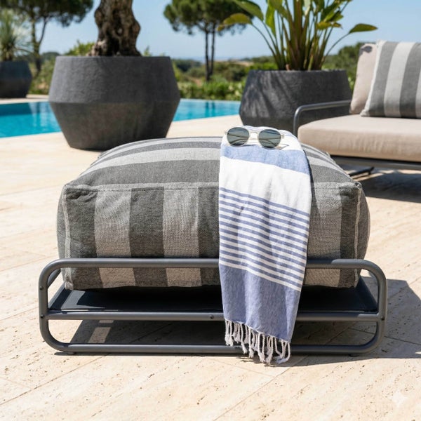 Gestreifter Outdoor-Hocker mit Metallgestell auf einer Terrasse am Pool, dekoriert mit einem Handtuch und einer Sonnenbrille.