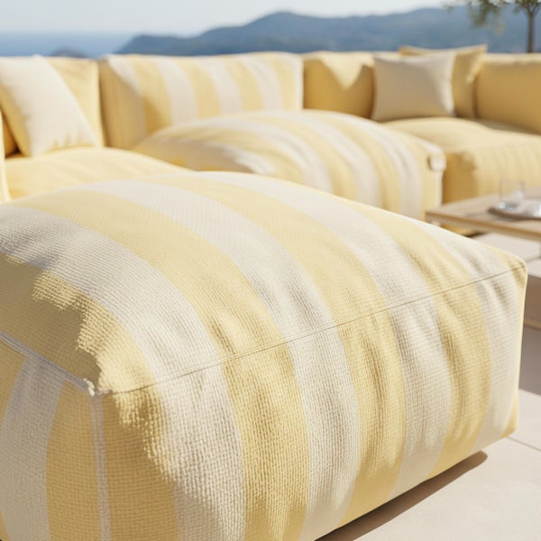 Moderne Gartenlounge mit gelben Polstern und Zierkissen auf einer hellen Fliesenterrasse direkt am Pool.