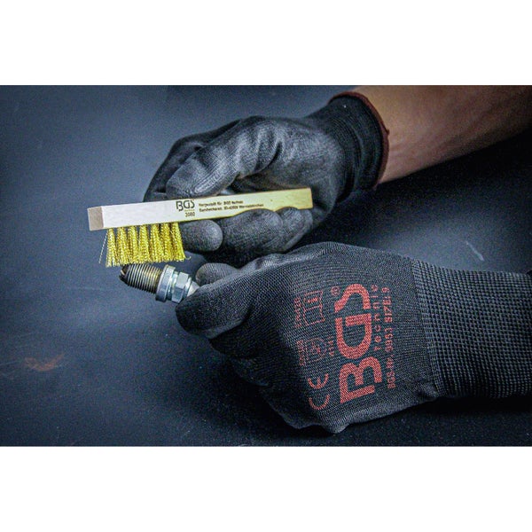 Eine Person reinigt eine Zündkerze mit einer Drahtbürste. Sie trägt dabei Handschuhe.