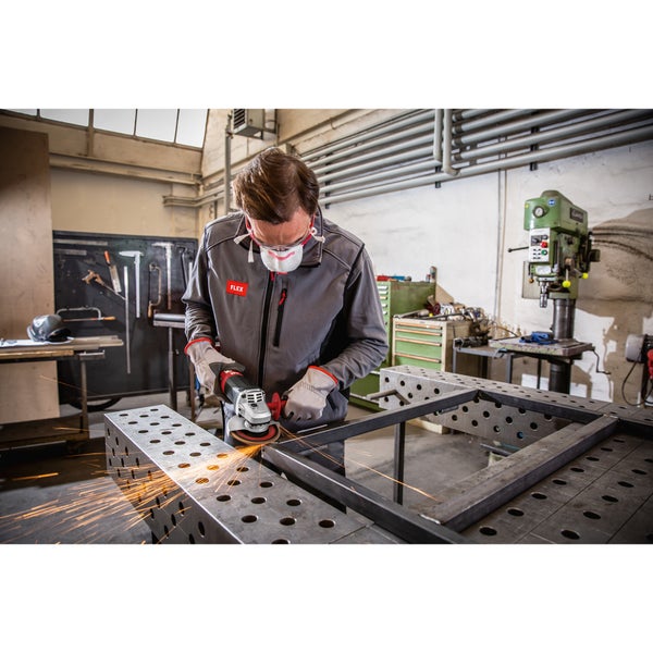Handwerker arbeitet in einer Werkstatt mit einem Winkelschleifer an einer Metallkonstruktion auf einem Schweißtisch mit Funkenschlag.