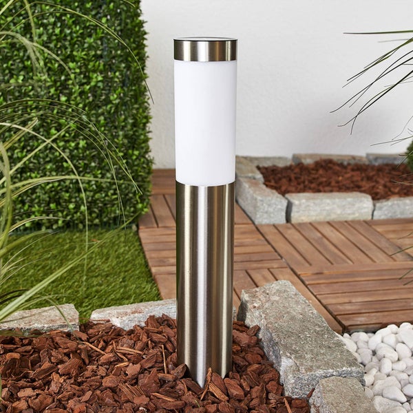 Moderne Edelstahl-Außenleuchte in Zylinderform mit weißem Kunststoffdiffusor in einem Garten mit Rindenmulch und Holzfliesen.