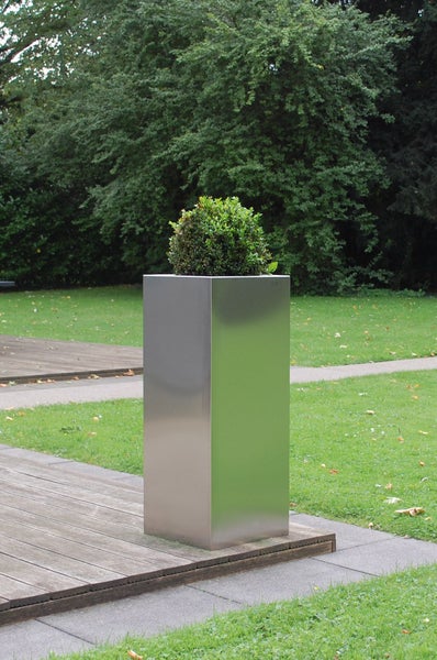 Hoher, quadratischer Pflanzkübel aus Edelstahl mit einem grünen Buchsbaum auf einer Holzterrasse im Garten.