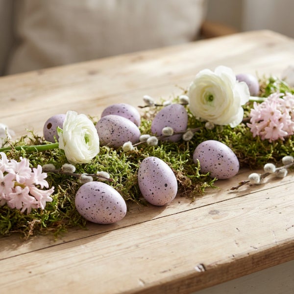 Osterdekoration auf einem Holztisch mit gesprenkelten Eiern, frischen Blumen und Weidenkätzchenzweigen als Tischschmuck.