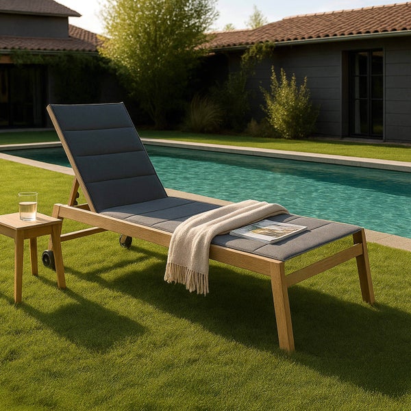 Sonnenliege aus Holz mit Polsterauflage und Rollen auf einer Rasenfläche neben einem Swimmingpool.