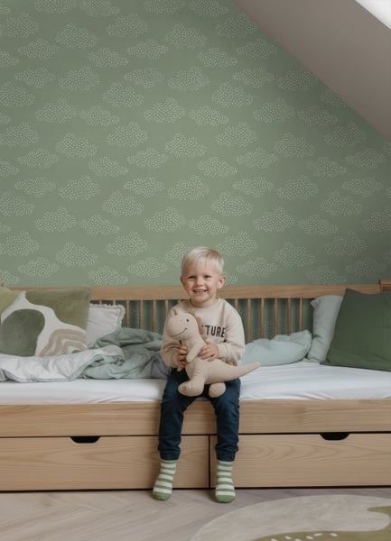 Vliestapete mit weißem Wolkenmuster auf grünem Grund in einem hellen Kinderzimmer mit Holzbett.