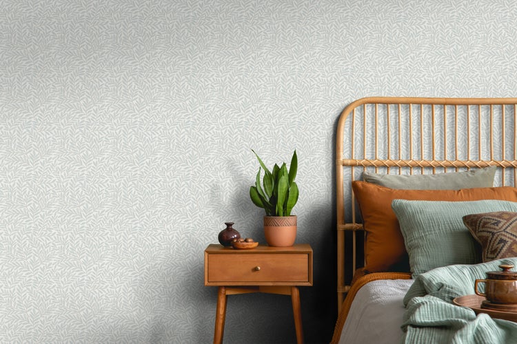 Schlafzimmer mit blattgemusterter Tapete, Rattankopfteil und Nachttisch.