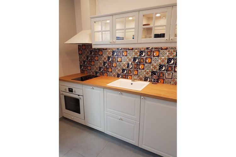 Küche mit weißen Schränken, Holzarbeitsplatte und farbenfrohen Fliesen