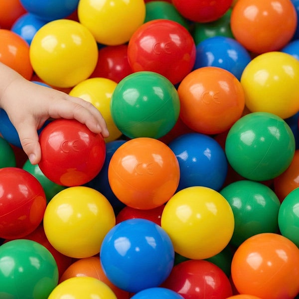 Kinderhand greift in eine Menge Bällebadbälle aus Kunststoff mit europäischer Konformitätskennzeichnung.