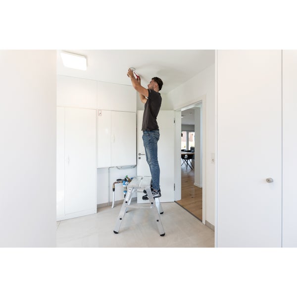Mann auf einer Trittleiter bei der Installation eines Rauchmelders im Innenbereich
