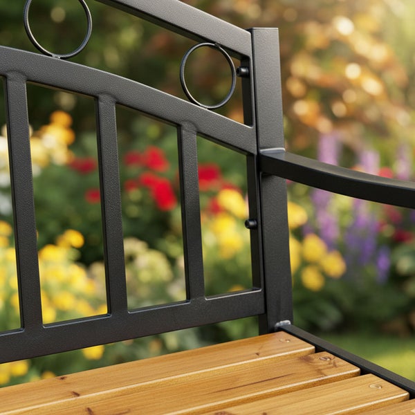 Detail einer Gartenbank mit einer Rückenlehne aus schwarzem Metall mit Kreisornamenten und einer Sitzfläche aus Holzlatten.