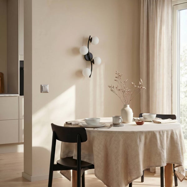 Moderne Wandleuchte mit vier Glaskugeln an schwarzer Halterung in hellem Esszimmer über einem gedeckten runden Tisch.