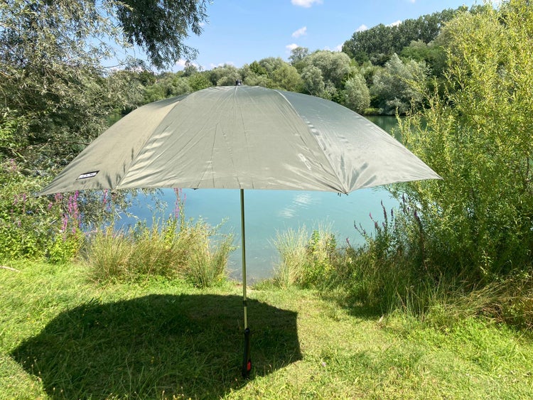 Olivegrüner Angelschirm auf einer Wiese am Seeufer als Wetterschutz.
