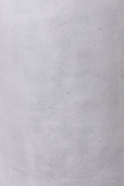 Hohes, ovales Pflanzgefäß in Betonoptik mit grüner Pflanze neben einer Haustür im Außenbereich.