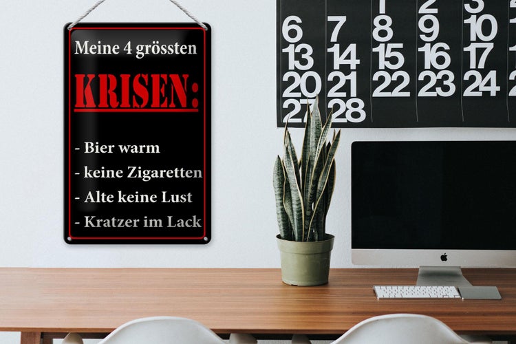 Blechschild Meine 4 grössten Krisen an einer Wand in einem hellen Arbeitszimmer neben Schreibtisch, Pflanze und Computer.