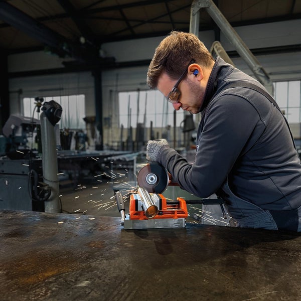 Handwerker mit Schutzausrüstung nutzt einen Fein Winkelschleifer zur Bearbeitung eines Metallprofils in einer Werkstatt.