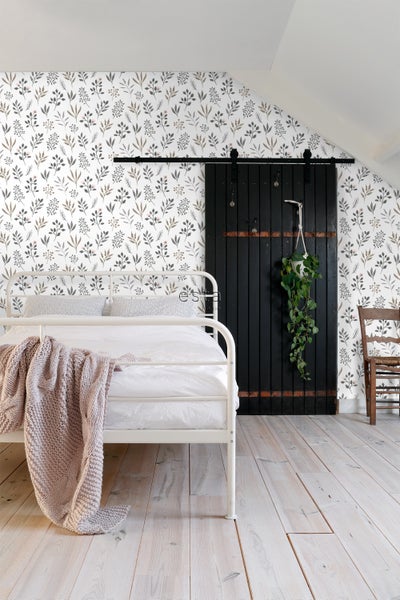 Schlafzimmer mit weißem Metallbett, floraler Tapete und dunkler Schiebetür