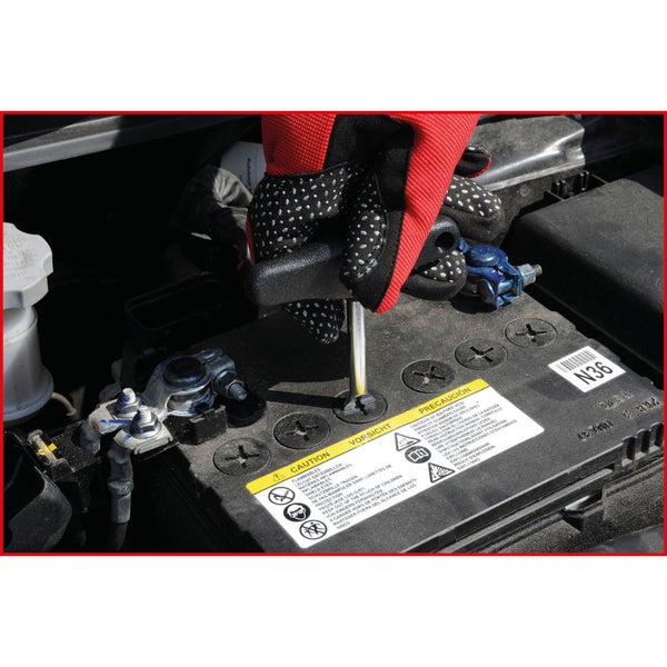 Eine Person mit Handschuhen verwendet einen Schraubenzieher an einer Autobatterie.