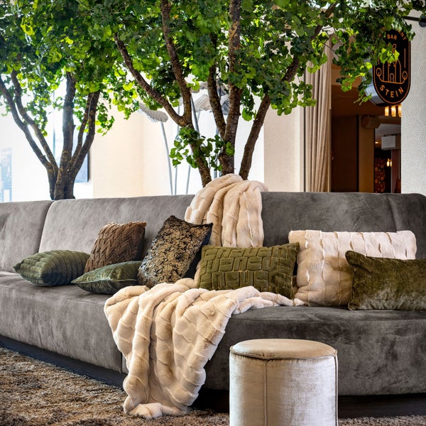 Graues Sofa dekoriert mit Kissen und Decken, ergänzt durch einen Hocker.