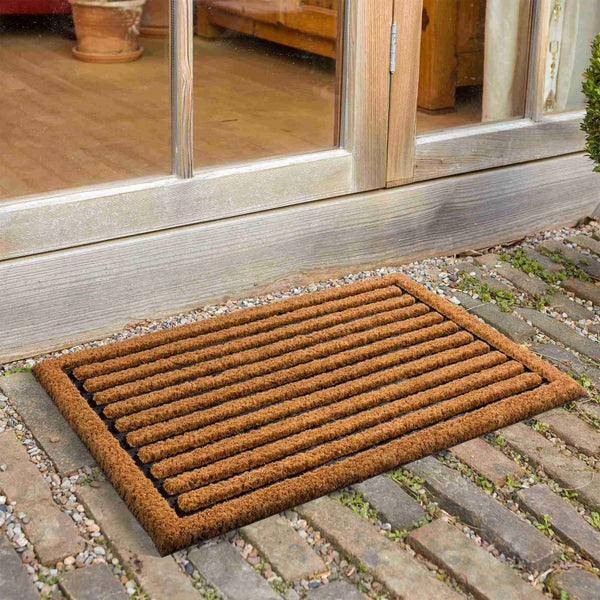 Fußmatte aus Kokosfasern vor einer Haustür auf Pflastersteinen