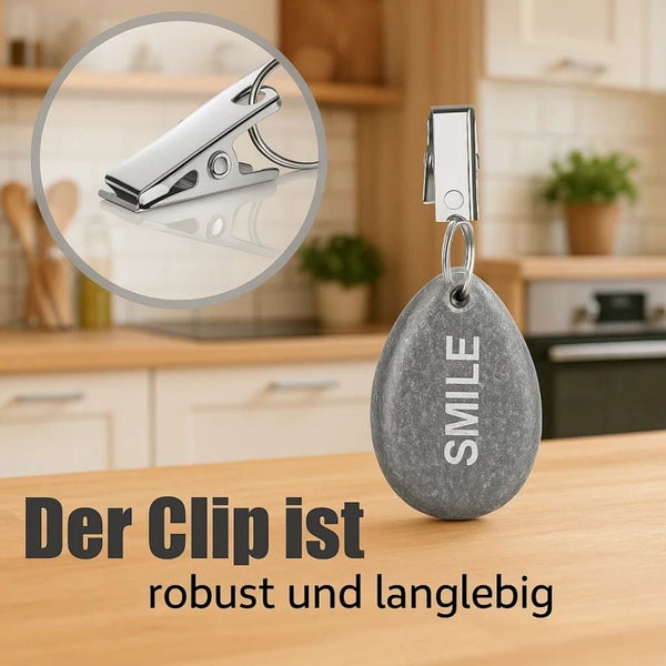 Tischdeckengewicht in Steinoptik mit Metallclip und Schriftzug Smile auf einem Holztisch in einer Küche.