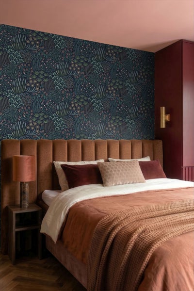 Schlafzimmer mit Doppelbett, braunem Samtkopfteil, dunkler botanischer Tapete, Nachttisch und gemütlichen Textilien.