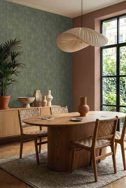 Modernes Esszimmer mit strukturierter Tapete in Grün, ovalem Massivholztisch, geflochtenen Holzstühlen und einer markanten Pendelleuchte.