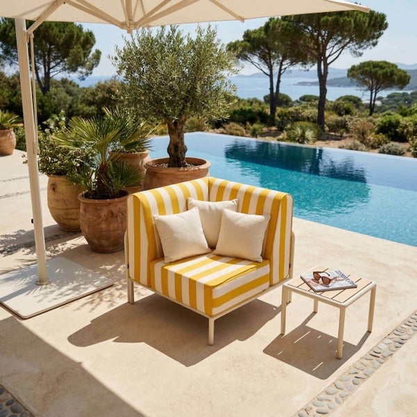 Gelb-weiß gestreifter Loungesessel mit weißen Kissen auf einer hellen Terrasse am Pool, inklusive Beistelltisch und Sonnenschirm.