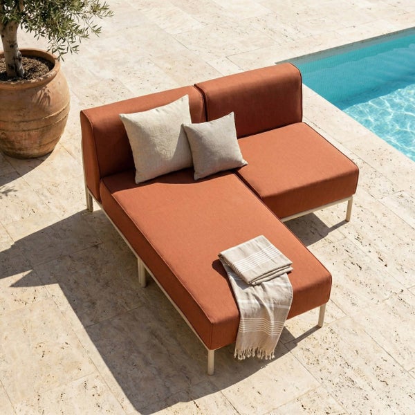Modernes Garten-Ecksofa mit rostfarbenen Polstern auf einer hellen Steinterrasse neben einem Pool.