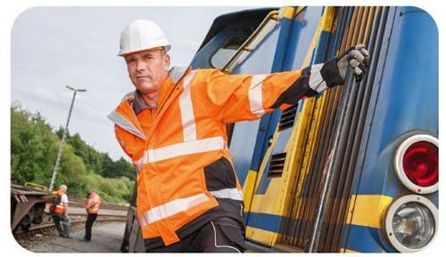 Ein Bauarbeiter in Warnschutzkleidung und Schutzhelm steht neben einem Zug auf einem Bahngelände.