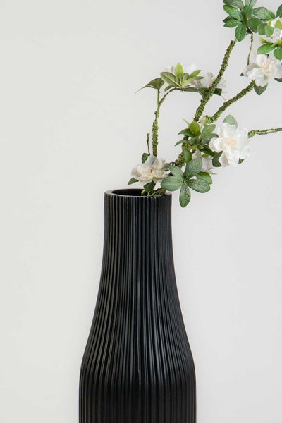 Schwarze geriffelte Vase mit künstlichen weißen Blumen und grünen Blättern.