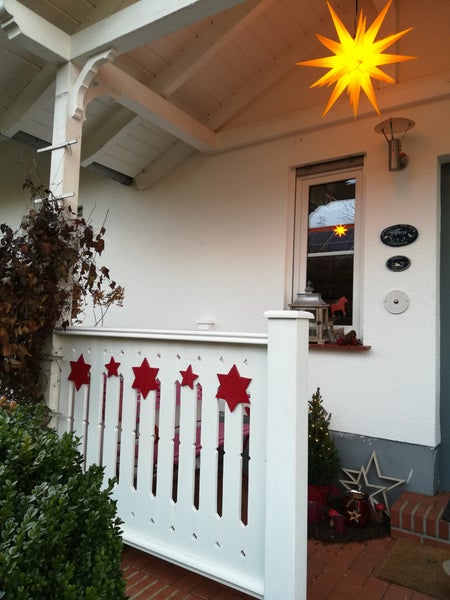 Weihnachtliche Terrassenveranda mit leuchtendem Stern und roter Sternendekoration am weißen Geländer.