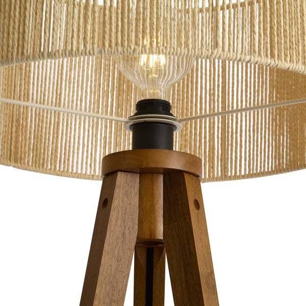 Nahaufnahme einer Dreibeinlampe mit braunem Holzfuß, schwarzer Fassung, klarem Leuchtmittel und naturfarbenem Schirm aus Papierseil.