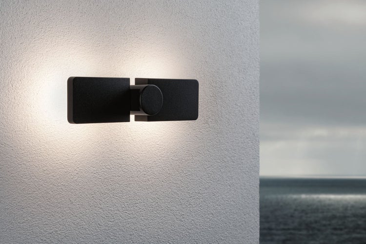 Moderne schwarze rechteckige Außenwandleuchte mit indirektem Licht an einer strukturierten Wand.